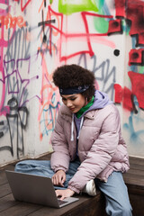 African american freelancer using laptop near graffiti on wall