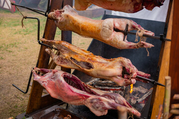 Process of cooking roasted pork carcasses on spit at summer outdoor food market. Professional cooking, catering, cookery, gastronomy and street food concept