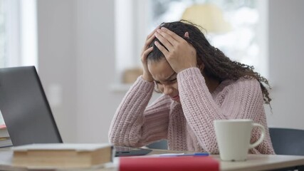 Tired teen girl rubbing temples having migraine headache studying online from home. Tired exhausted African American teenage student on remote education during coronavirus lockdown
