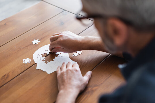 Blurred man with dementia folding jigsaw on table at home
