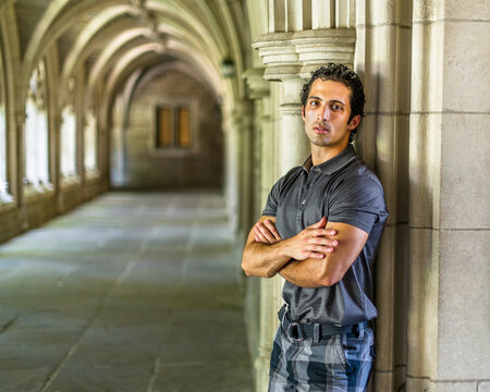 A young strong handsome guy is standing by a old fashion hall way, crossing arms and thoughtfully looking at you. - Powered by Adobe