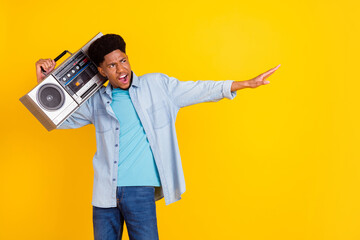 Photo of cool cute dark skin man wear jeans shirt listening boombox singing looking empty space isolated yellow color background