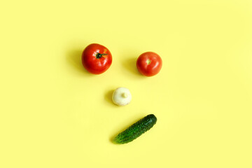 Vegetable face on a yellow background tomato eyes, garlic nose, cucumber grin, ingredients top view, copy space.