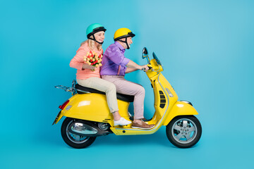 Portrait of attractive cheerful couple riding bike carrying flowers having fun isolated over bright blue color background