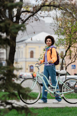 Fototapeta na wymiar Young african american woman with bike and backpack looking at camera on urban street