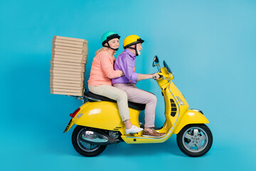Fototapeta na wymiar Portrait of two cheerful elderly retired pensioners riding moped delivering fastfood isolated over bright blue color background