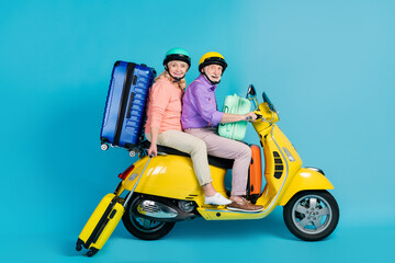 Fototapeta na wymiar Portrait of two cheerful elderly retired pensioners riding moped carrying bags tour isolated over bright blue color background