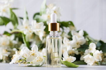 Obraz na płótnie Canvas Jasmine essential oil in a glass dropper on a background of jasmine flowers.