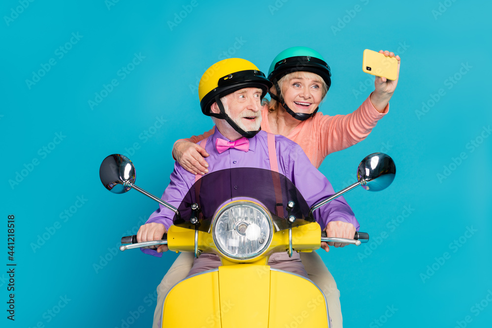 Poster Photo of grey haired retired pensioner husband wife couple people wear helmet rider make selfie isolated on blue color background