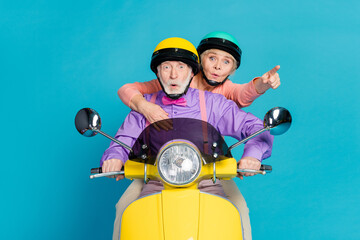 Photo of retired pensioner husband wife ride motorbike point finger amazed shocked isolated on blue...