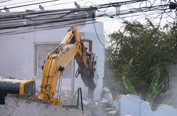 big yellow excavator removal home building by destroy concrete wall. uproot old construction house for development new project.