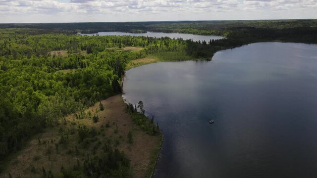 4K flyover of blue, rippling lake with green treed shoreline and forests surrounding it. Pontoon boat can be seen on lake. Lake Itasca, MN. Wide view.