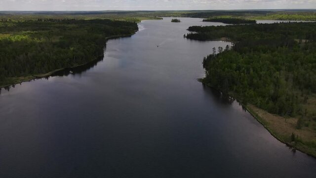 4K flyover of blue, rippling lake with green treed shoreline and forests surrounding it. Multiple boats can be seen on water. Lake Itasca, MN. Wide view.