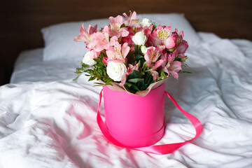 a pink box with fresh spring flowers stands on a snow-white bed