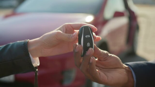 Close up of female seller presenting keys from red electric car to male customer. Blur background of luxury auto. Concept of successful deal. Female seller giving keys from electric car to male client