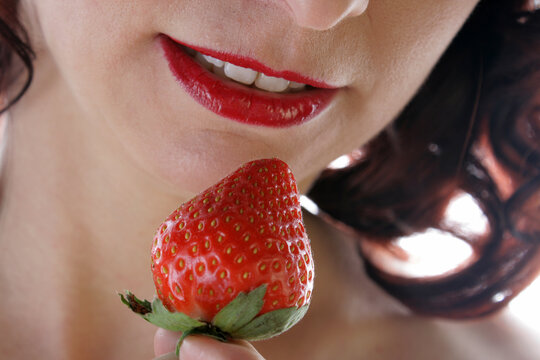Eine rote Erdbeere am Mund einer Frau