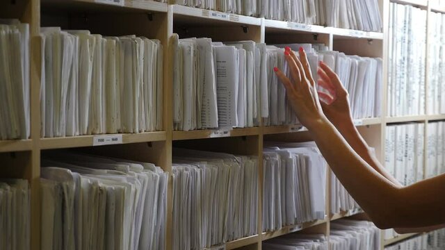 Paper files with notes in clinic. Old fashioned traditional medical cards on shelves in hospital. Female hands sorting folders in drawer for papers. Medical Archive and Search for Medical Documents. 4
