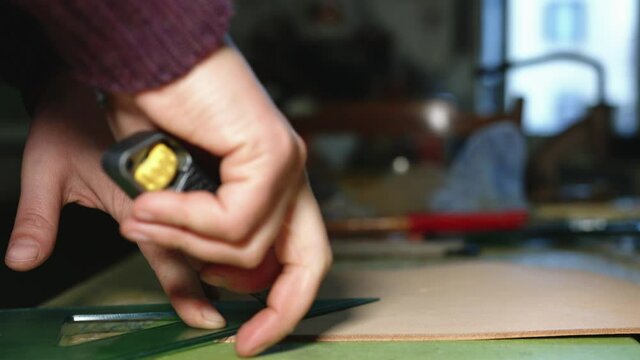 Leather craftsman at work. Close up of his hands cutting leather using a cutter