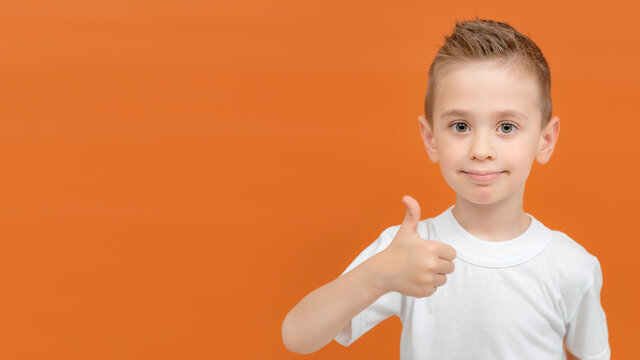 Banner portrait of happy preschooler boy showing thumbs up gesture isolated on orange background. Copy space for your text or product