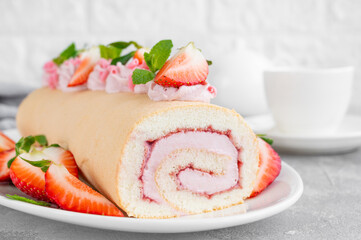 Cake roll with fresh strawberries, jam and cream cheese on a white plate on a gray background. Copy space.