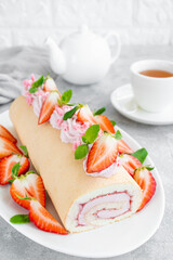Cake roll with fresh strawberries, jam and cream cheese on a white plate on a gray background. Copy space.