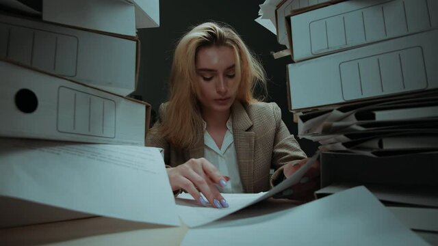 Tired woman with pile of folders working in office, female employee works with documents in evening having headache, exhausted worker with red eyes reading documentation. Fatigue, lots of work. 