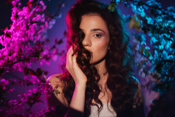 A fantastic shot of a girl in flowers looking like a nymph with a neon colored light. Close-up. The concept of fantasy, fairy tales, magic and fairies.
