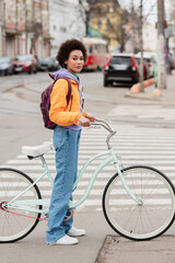 Young african american woman standing near bike on road on urban street