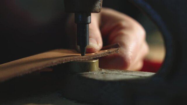 Leather craftsman at work. Close up of his hands using a hand rivet press in order to puncture leather