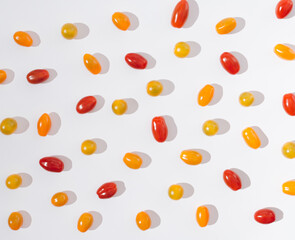 A cute pattern or wallpaper made of red, orange and yellow cherry tomatoes on a white background. Happy summer food or summer vibes concept.