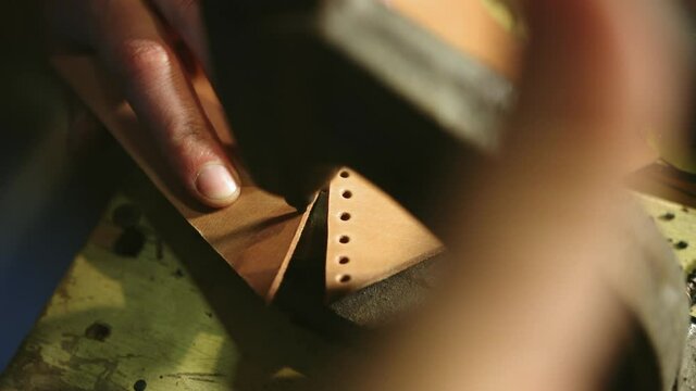 Leather craftsman at work. Top view Close up of his hands using a hand rivet press in order to puncture leather