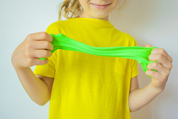 Hands with green slime close up. A child in a yellow t-shirt stretching slime. Trendy liquid toy...