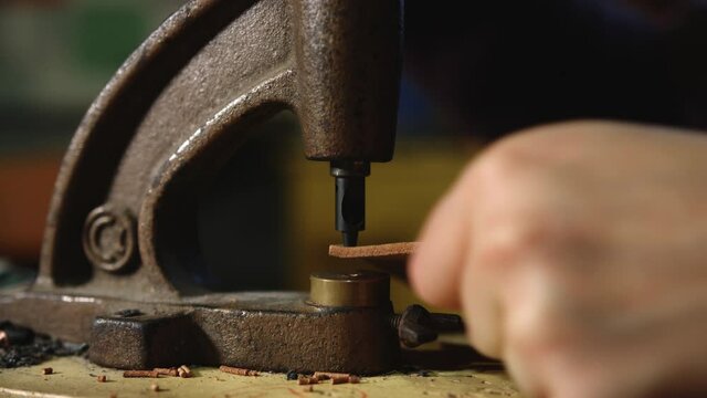 Leather craftsman at work. Extreme Close up of his hands using a hand rivet press in order to puncture leather