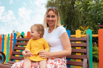 Happy children's Day. Portrait of a young happy mother with a little daughter in her arms. In the background, a colorful fence. Family planning concept