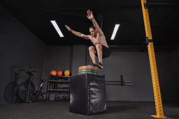 Crossfit athlete doing box jump exercise as part of functional circuit training at dark gym. Strong...