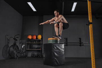 Portrait of an athletic man doing box jump exercise. Crossfit, sport and healthy lifestyle concept. Shot of a young man train jumping onto box as part of exercise routine. Cross, functional training