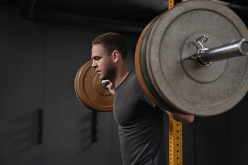 Portrait of male bodybuilder doing back squats in gym. Muscular handsome young man getting ready to...