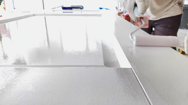 The painter at work paints the wooden door with white paint with a paint roller.  Professional painting services