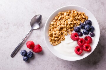 A white bowl with plain yogurt garnished with ripe blueberries and raspberries and granola oatmeal