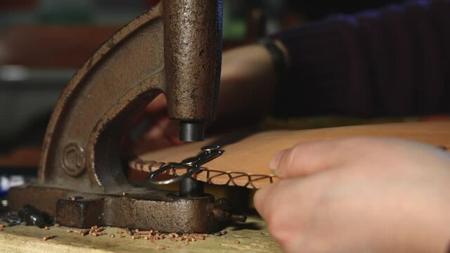 Leather craftsman at work. Close up of his hands using a hand rivet press in order to insert metal button