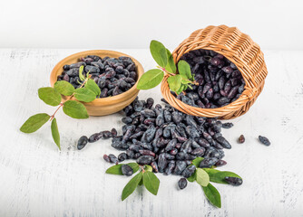 Ripe honeysuckle berries in a basket and in a saucer on a white background top view