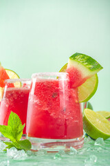 Cold summer cocktail, watermelon margaritas or mojito with watermelon and lime slices, crushed ice and mint. Seasonal refreshing drink, on bright green sun lighted background