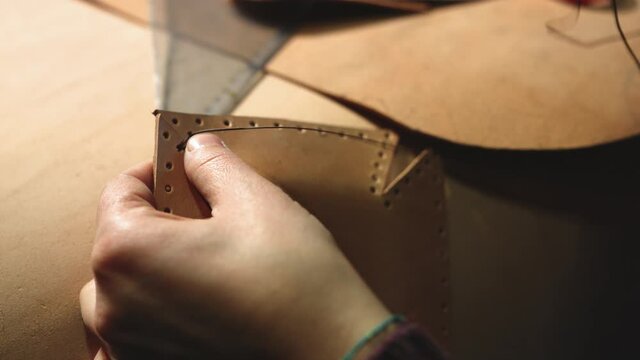 Leather craftsman at work. Close up of his hands stitching the pocket of a bag