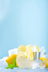 Traditional summer cold refreshing cocktail lemonade, with lemon slices and lots of crushed ice and iced pedestals on blue background