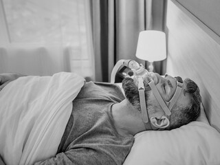 Monochrome portrait of Sleeping man with chronic breathing issues considers using CPAP machine in...