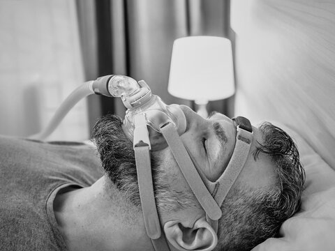 Monochrome portrait of Sleeping man with chronic breathing issues considers using CPAP machine in bed. Healthcare, Obstructive sleep apnea therapy, CPAP, snoring concept