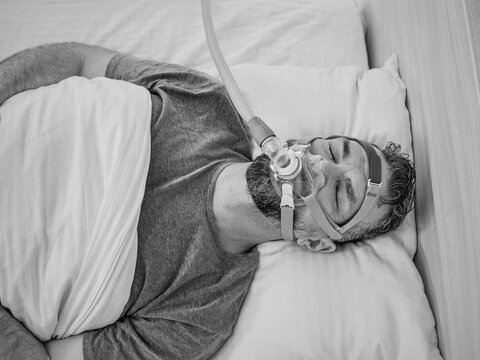 Monochrome portrait of Sleeping man with chronic breathing issues considers using CPAP machine in bed. Healthcare, Obstructive sleep apnea therapy, CPAP, snoring concept