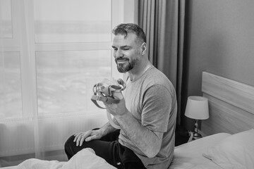 Mature happy man with chronic breathing issues considers using CPAP machine sitting on the bed in bedroom . Healthcare, CPAP, snoring concept