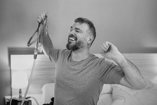 monochrome portrait of Happy rested man with chronic breathing issues after using  CPAP machine sitting on the bed in bedroom. Healthcare, CPAP, Obstructive sleep apnea therapy, snoring concept