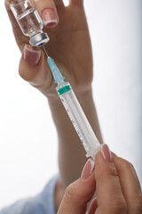 Doctor woman in facial mask medicine dials vaccine into syringe isolated on white background.